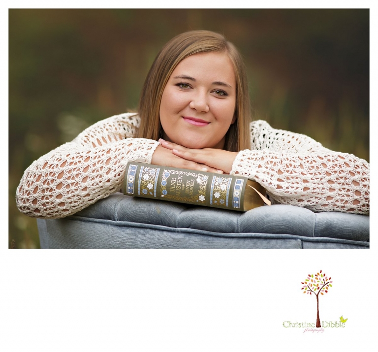 Sonora and Summerville senior portrait photographer Christine Dibble Photography takes outdoor senior portraits of a girl leaning on the back of a velvet chair with her books in a wildflower field.