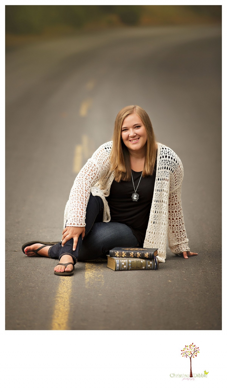 Sonora and Summerville senior portrait photographer Christine Dibble Photography takes outdoor senior portraits of a girl sitting on the ywllow line in the road with her books.