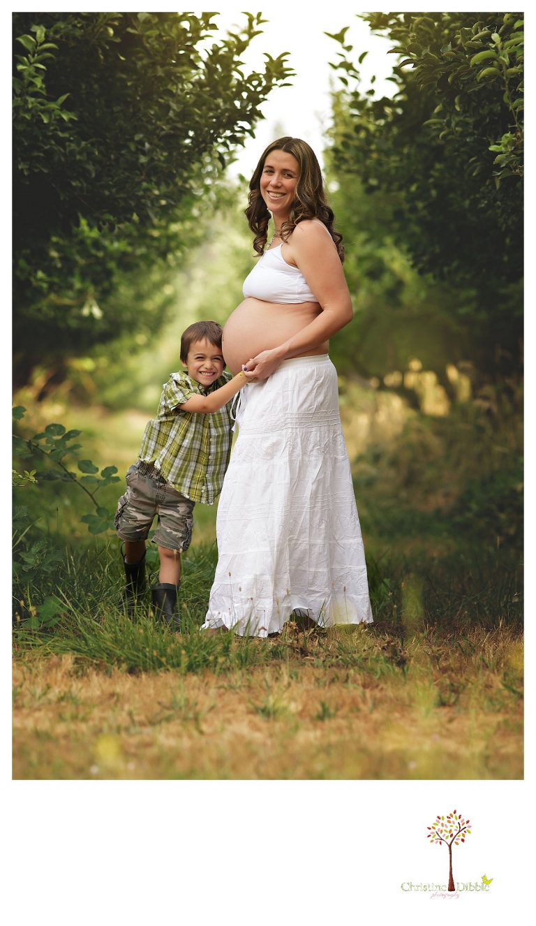 Sonora maternity photography session by Christine Dibble Photography shows a pregnant woman playing with her older son among apple trees.