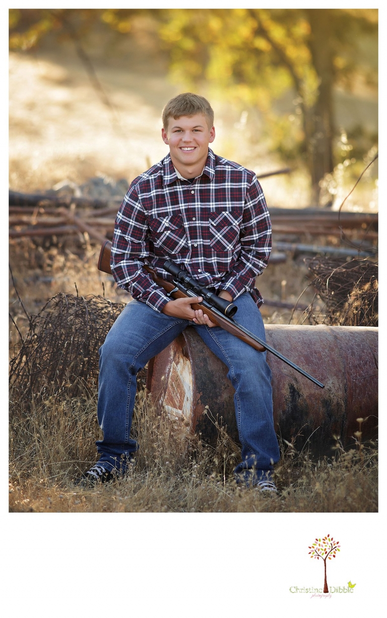 Summerville senior portrait photographer, Christine Dibble Photography of Sonora, photographs a boy with hig gun as he sits on a rusted barrel.