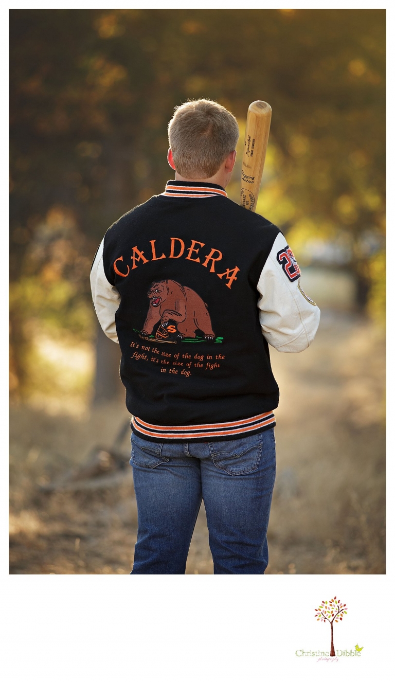 Summerville senior portrait photographer, Christine Dibble Photography of Sonora, takes portraits in the golden hour of a Summerville baseball player in his letterman jacket with his bat as he looks away.