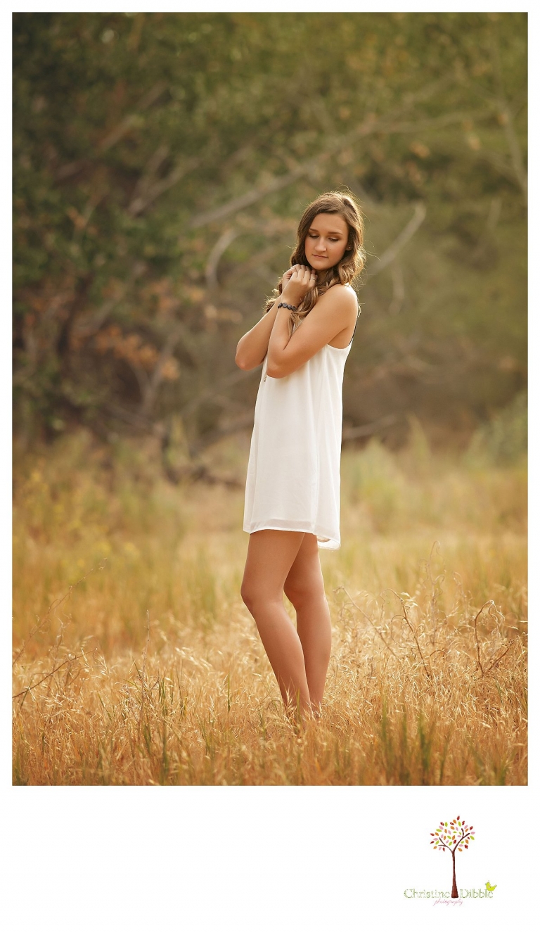 A senior girl stands in a grass field as Summerville and Sonora senior portrait photographer Christine Dibble Photography takes photos of her.
