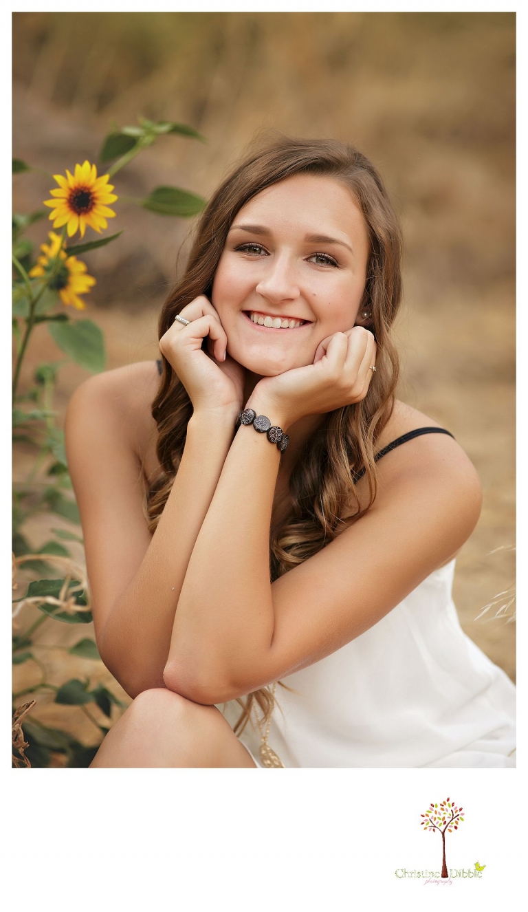 As she sits among small sunflowers, a senior girl is photographed by Summerville and Sonora senior portrait photographer Christine Dibble Photography.
