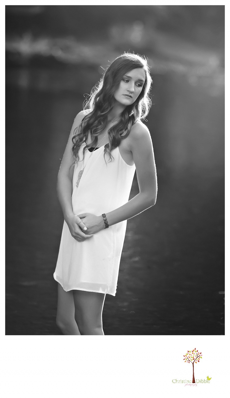 A black and white image is taken by Summerville and Sonora senior portrait photographer Christine Dibble Photography of a senior girl standing in the river in sunset light.