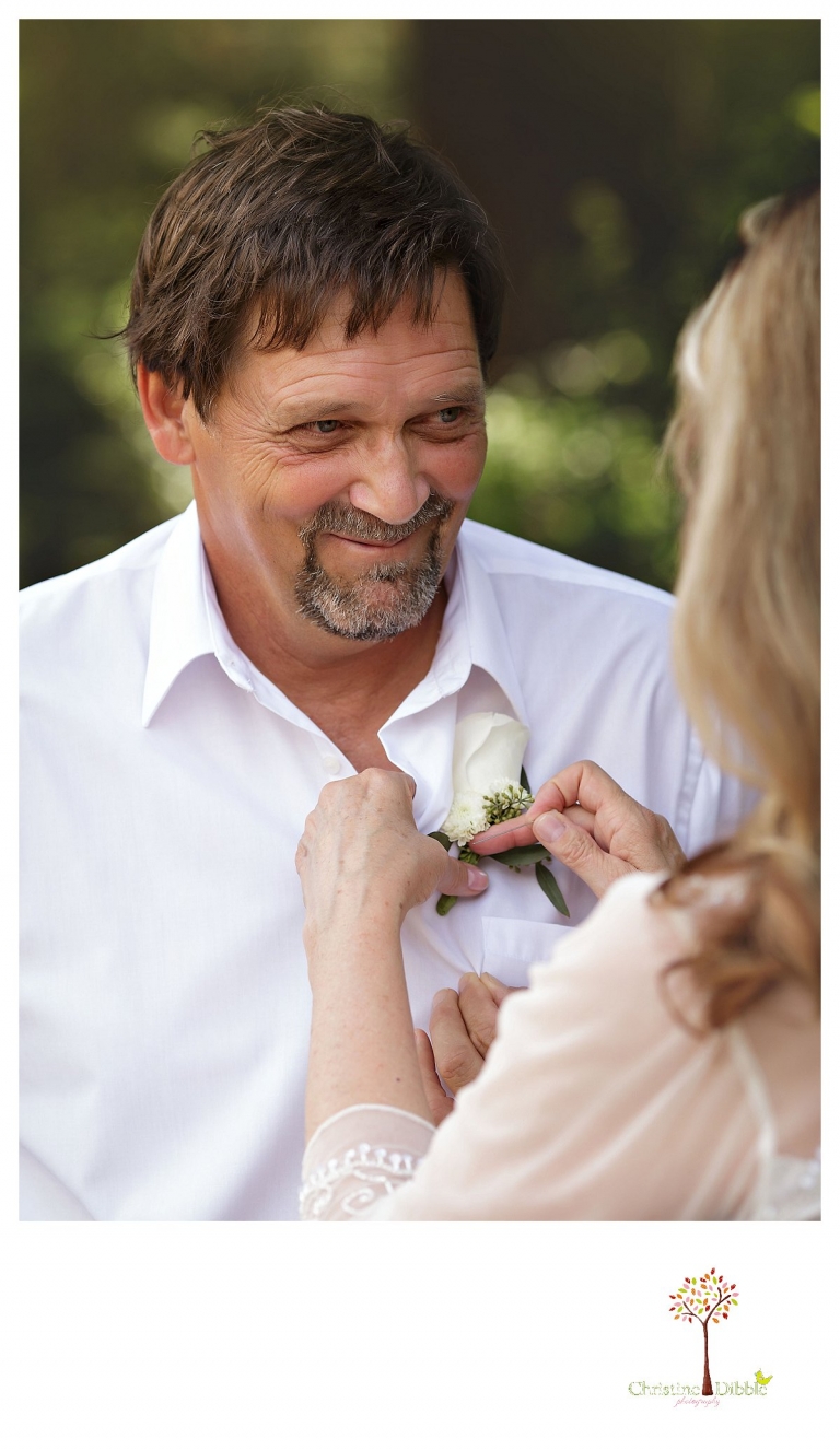 Wedding photography in Sonora by Christine Dibble Photography documents the groom looking at his bride as she pins on his boutonniere at Twain Harte Tree Farm before their wedding.