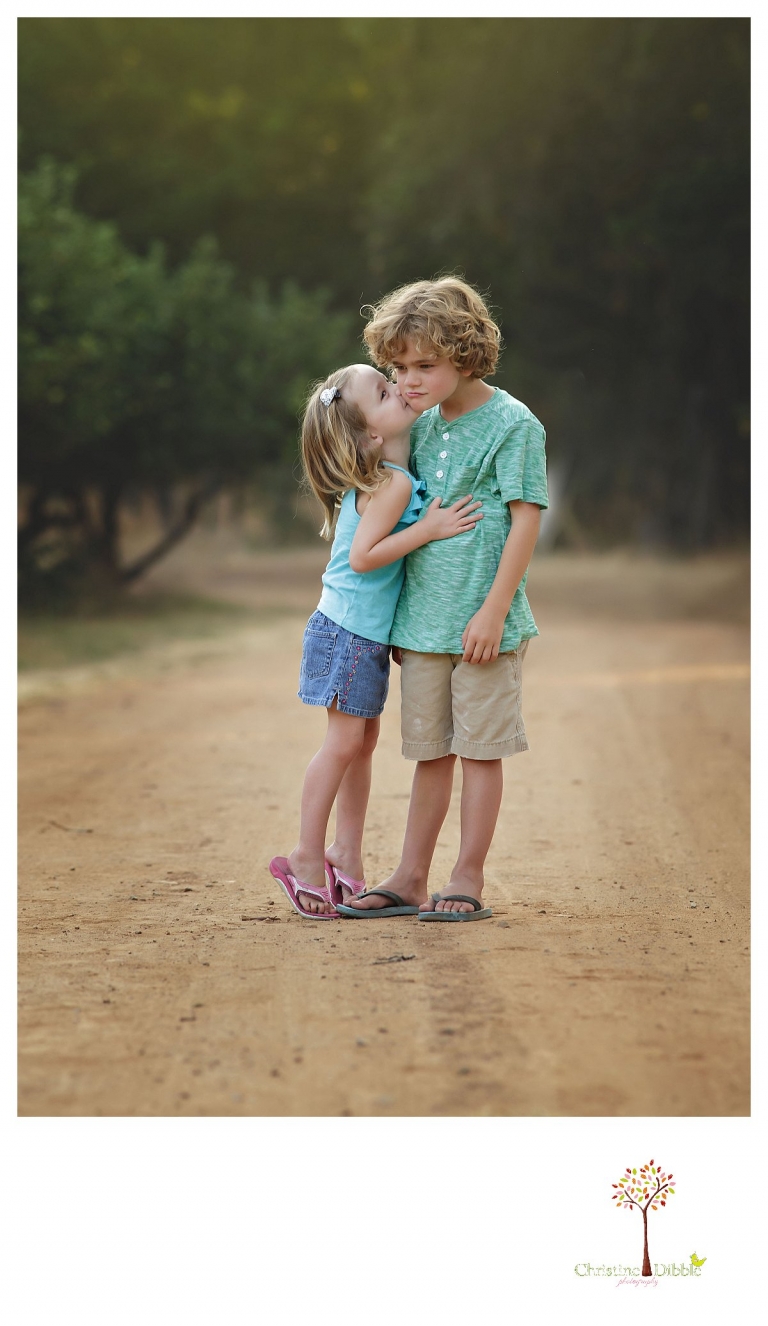 Sonora family photographer Christine Dibble Photography takes a photo of a younger sister kissing her pouting brother at Indigeny during a family portrait session.