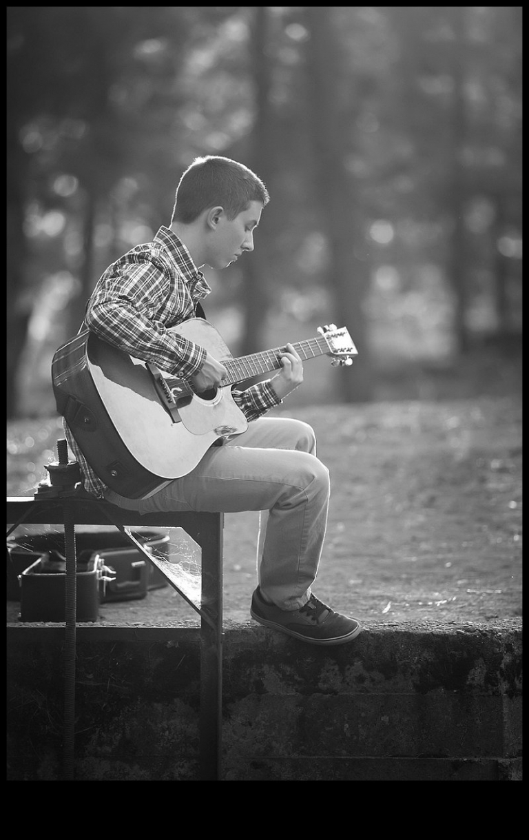 A senior boy plays his guitar on the bank of a river during a senior portrait session with Christine Dibble Photography of Sonora.