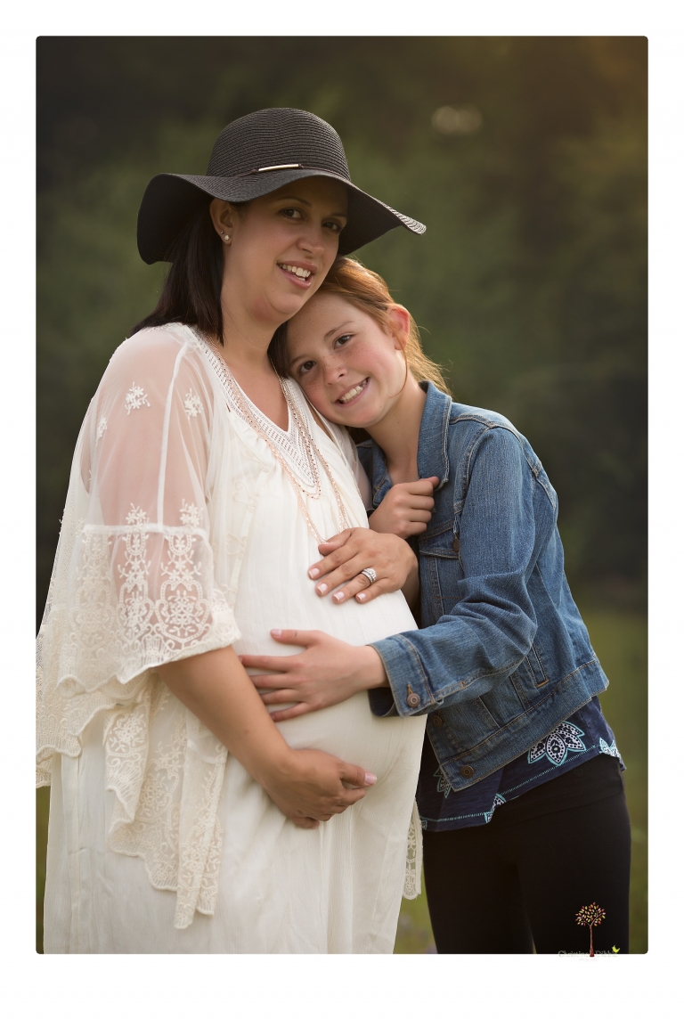 Sonora Maternity Photographer Christine Dibble Photography takes beautiful belly portraits of a mom-to-be pregnant with her fourth child in a white dress and floppy sunhat as she poses with her preteen daughter in a field of Lupine in Twain Harte.