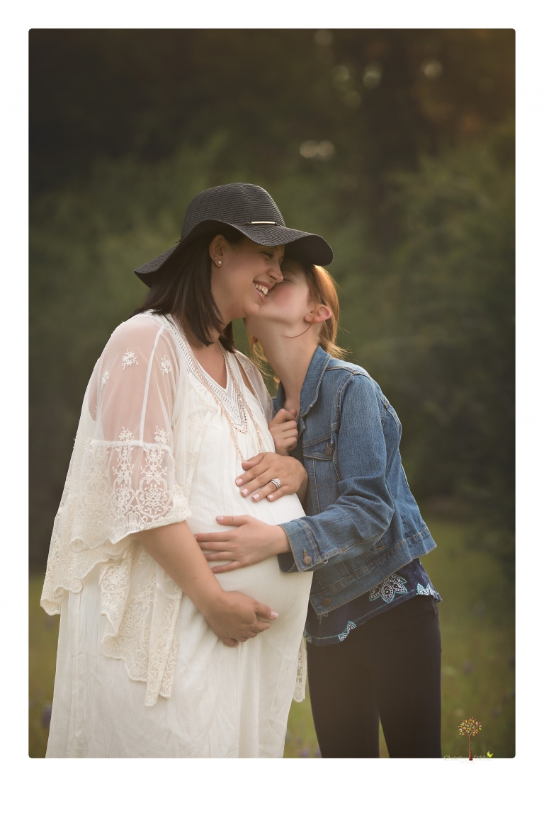 Sonora Maternity Photographer Christine Dibble Photography takes beautiful belly portraits of a mom-to-be pregnant with her fourth child in a white dress and floppy sunhat as she poses with her preteen daughter in a field of Lupine in Twain Harte.