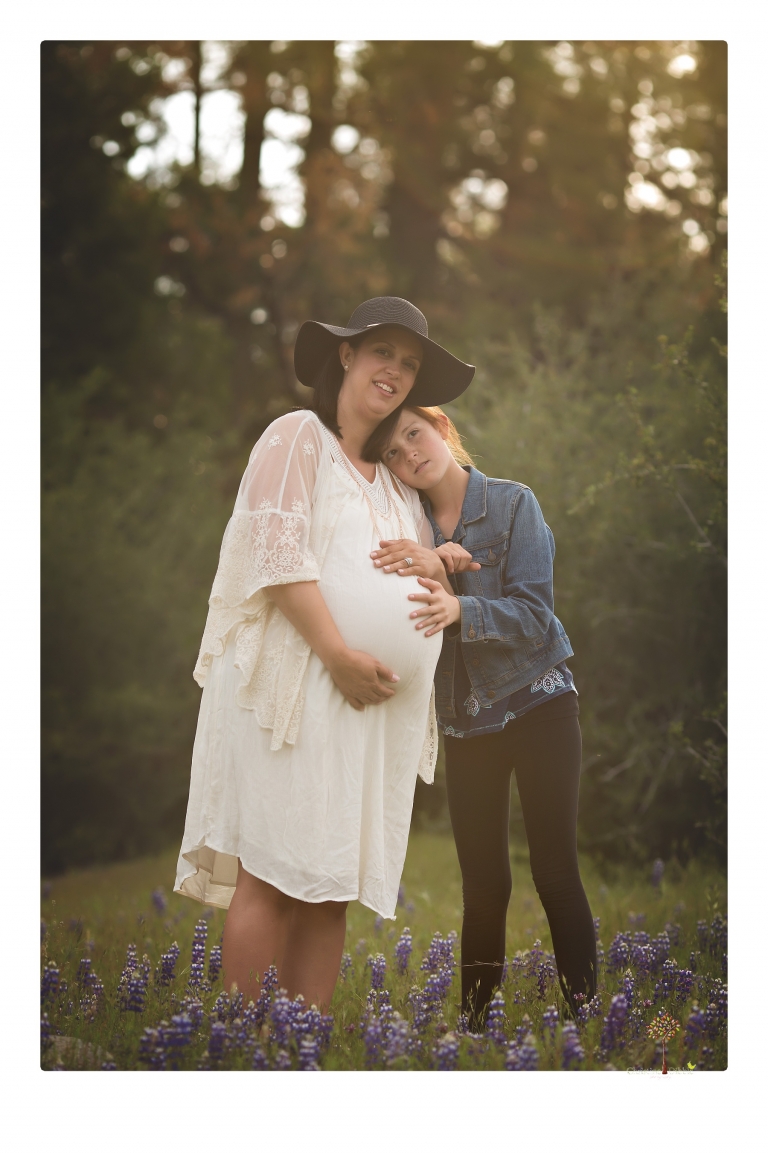 Sonora Maternity Photographer Christine Dibble Photography takes beautiful belly portraits of a mom-to-be pregnant with her fourth child in a white dress and floppy sunhat as she poses with her preteen daughter in a field of Lupine in Twain Harte.