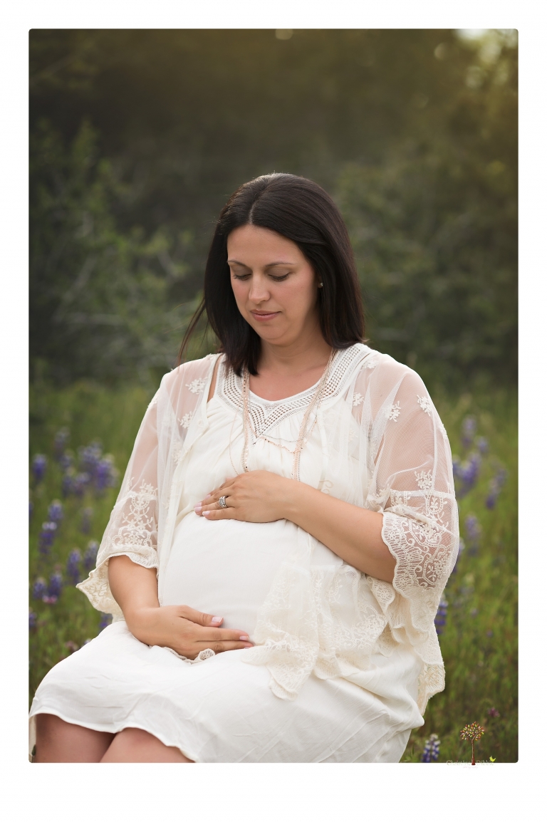 Sonora Maternity Photographer Christine Dibble Photography takes beautiful belly portraits of a mom-to-be pregnant with her fourth child in a white dress and floppy sunhat as she poses  in a field of Lupine in Twain Harte.