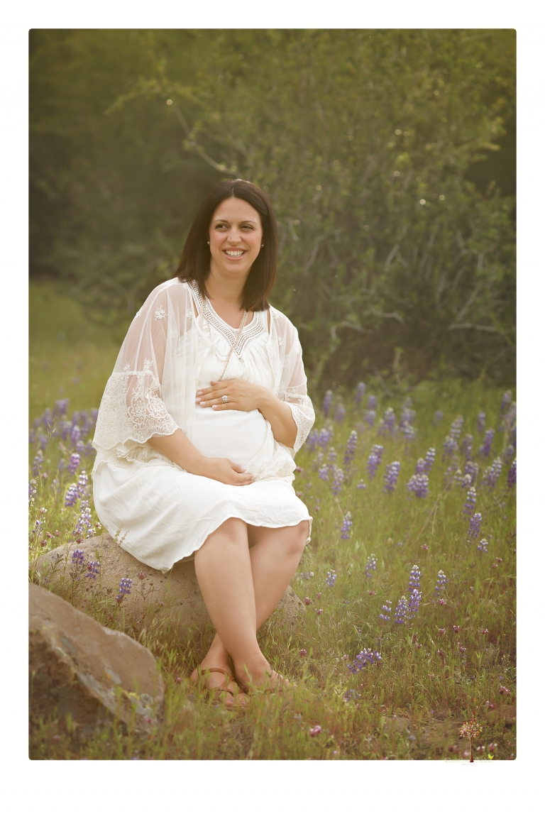 Sonora Maternity Photographer Christine Dibble Photography takes beautiful belly portraits of a mom-to-be pregnant with her fourth child in a white dress and floppy sunhat as she poses  in a field of Lupine in Twain Harte.