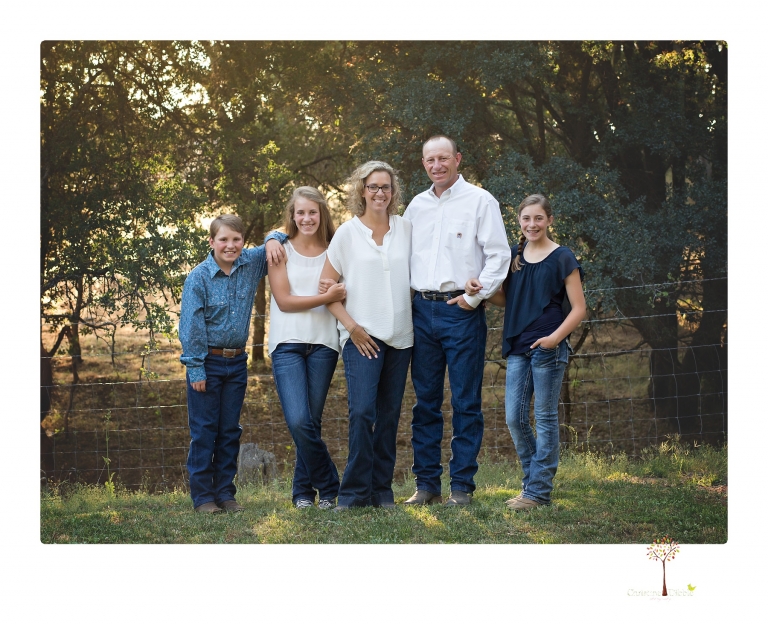 Sonora graduation photographer Christine Dibble Photography takes eighth grade graduation portraits of a girl in a pink lace dress, jeans and cowboy boots with her family, dogs, and steer, Big Mac in her family's yard.