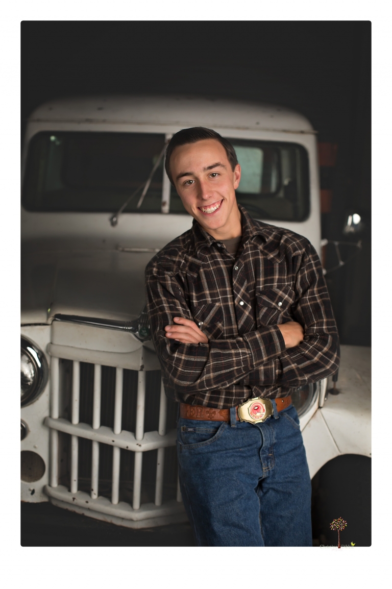 Summerville Senior Portraits taken by Christine Dibble Photography of Sonora in the auto shop with a senior boy's 1959 Jeep Willys pick-up truck and his letterman jacket.