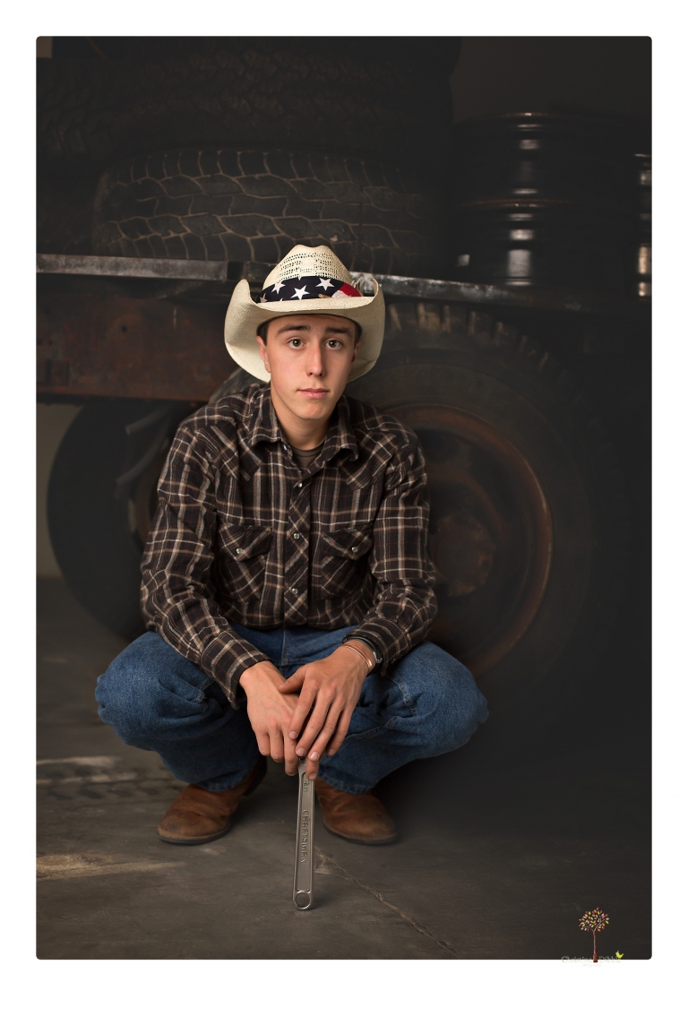 Summerville Senior Portraits taken by Christine Dibble Photography of Sonora in the auto shop with a senior boy's 1959 Jeep Willys pick-up truck and his letterman jacket.