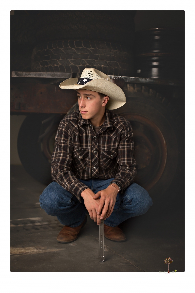 Summerville Senior Portraits taken by Christine Dibble Photography of Sonora in the auto shop with a senior boy's 1959 Jeep Willys pick-up truck and his letterman jacket.