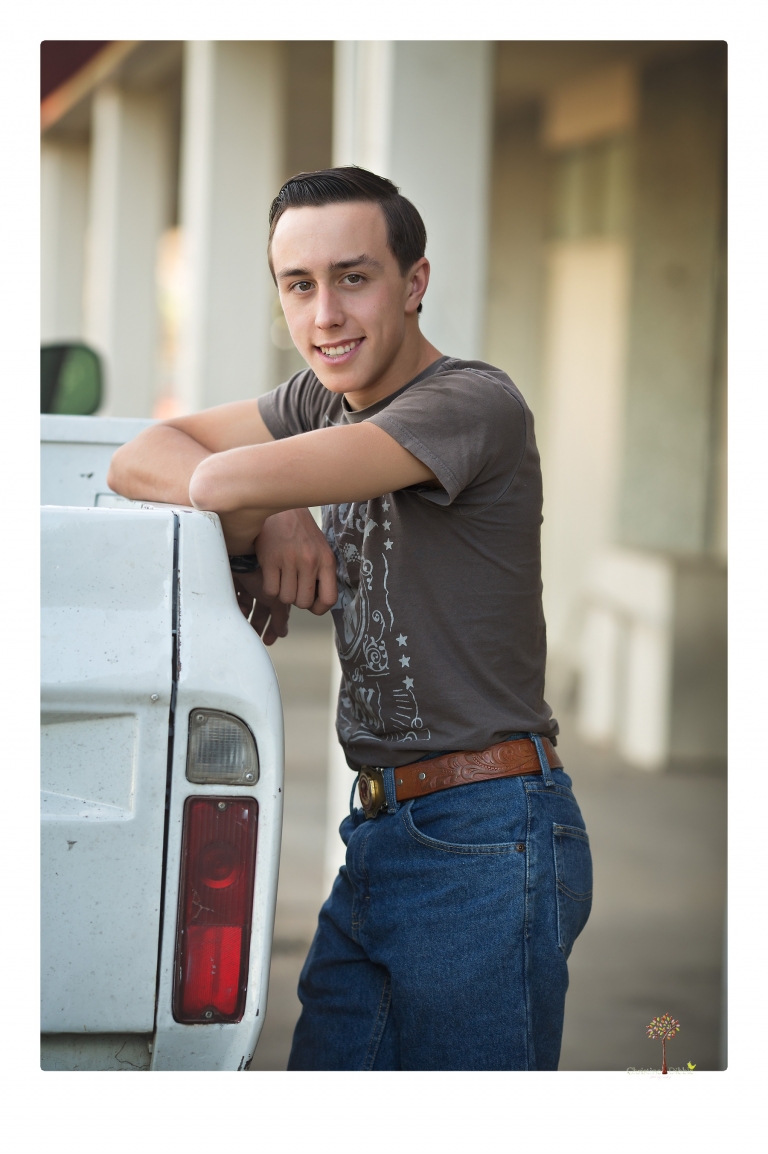 Summerville Senior Portraits taken by Christine Dibble Photography of Sonora in the auto shop with a senior boy's 1959 Jeep Willys pick-up truck and his letterman jacket.