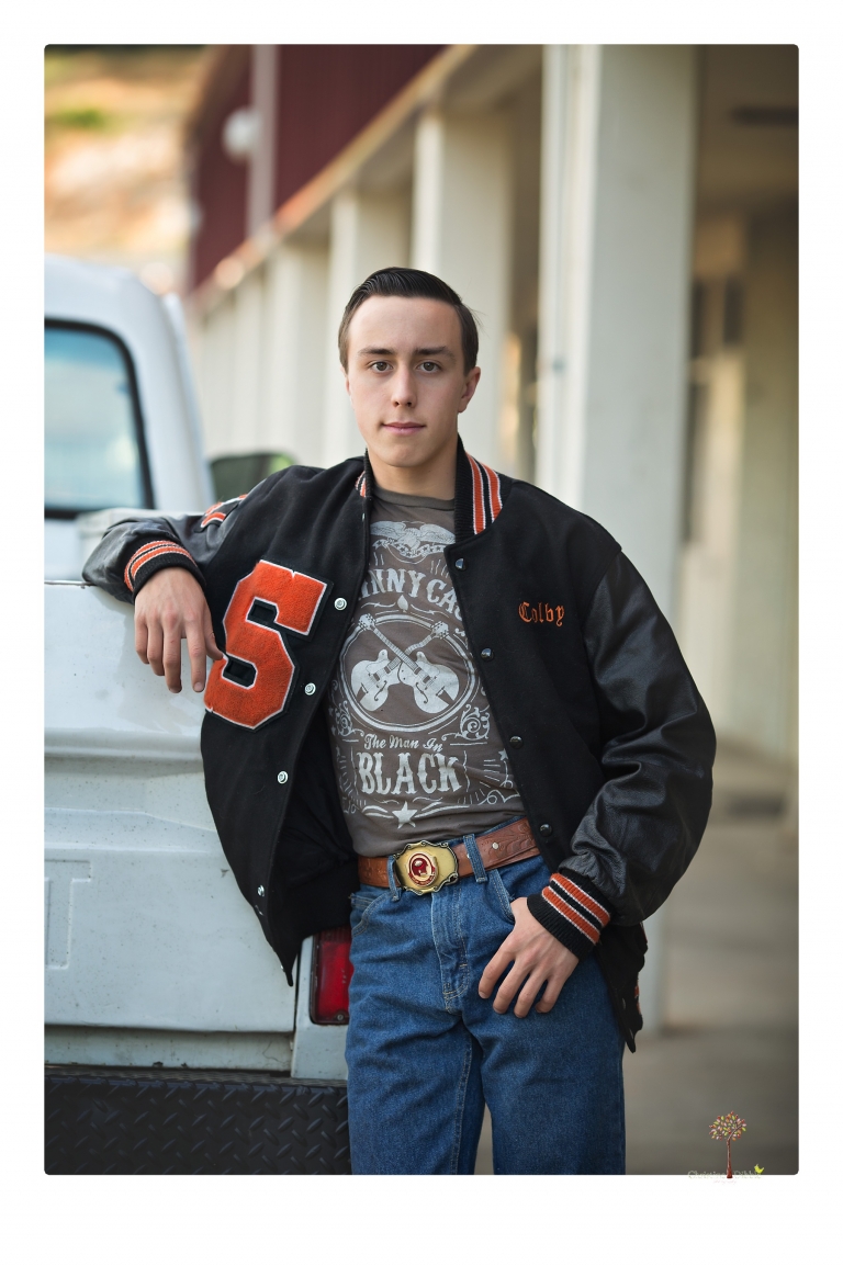Summerville Senior Portraits taken by Christine Dibble Photography of Sonora in the auto shop with a senior boy's 1959 Jeep Willys pick-up truck and his letterman jacket.