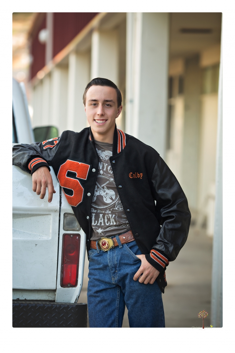Summerville Senior Portraits taken by Christine Dibble Photography of Sonora in the auto shop with a senior boy's 1959 Jeep Willys pick-up truck and his letterman jacket.