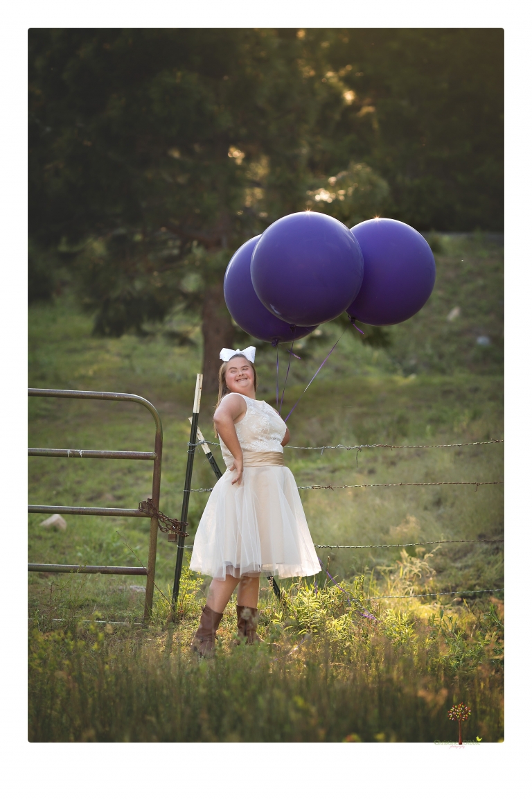 Sonora senior portrait photographer Christine Dibble Photography takes senior portraits of a girl in a lace dress with giant balloons on a velvet loveseat in a field.