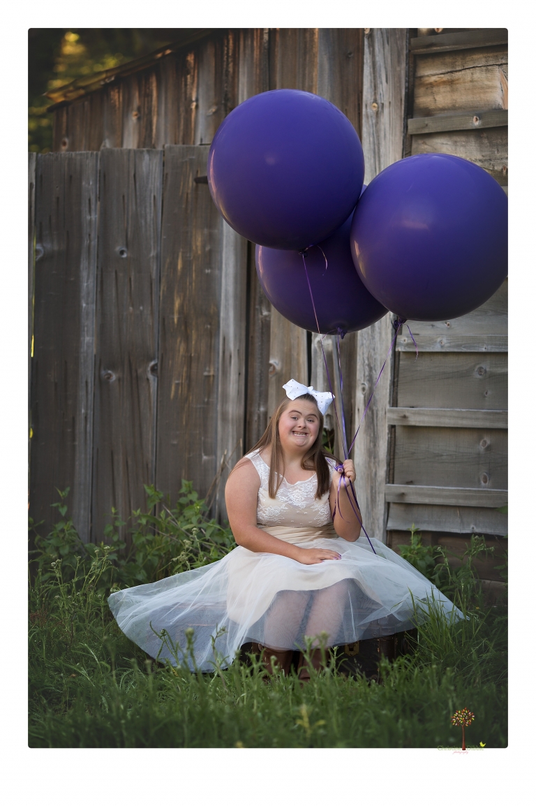 Sonora senior portrait photographer Christine Dibble Photography takes senior portraits of a girl in a lace dress with giant balloons on a velvet loveseat in a field.