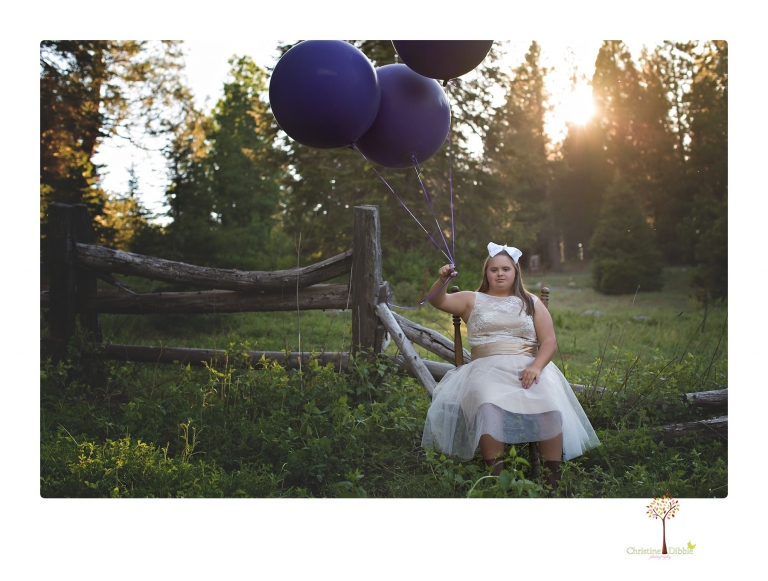 Sonora senior portrait photographer Christine Dibble Photography takes senior portraits of a girl in a lace dress with giant balloons on a velvet loveseat in a field.