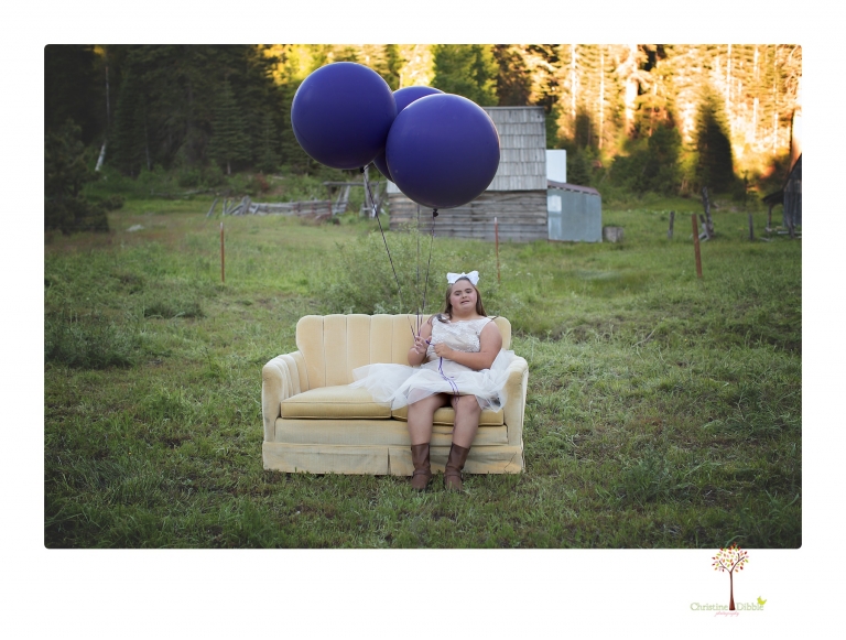 Sonora senior portrait photographer Christine Dibble Photography takes senior portraits of a girl in a lace dress with giant balloons on a velvet loveseat in a field.