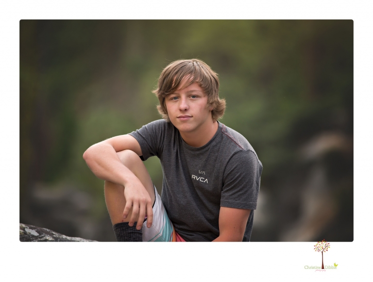 Summerville High School Senior portrait photographer Christine Dibble Photography takes four wheeling senior portraits of a boy with his trap gun, letterman jacket, and Toyota 4Runner as he drives over rocks and dives off cliffs.