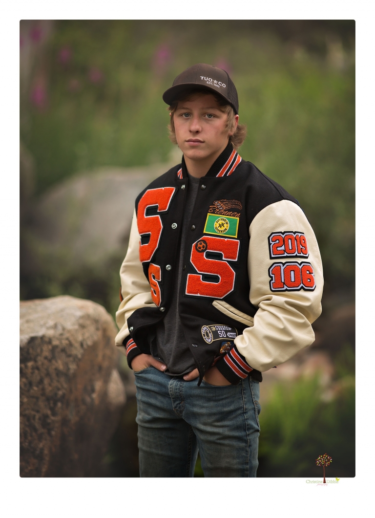 Summerville High School Senior portrait photographer Christine Dibble Photography takes four wheeling senior portraits of a boy with his trap gun, letterman jacket, and Toyota 4Runner as he drives over rocks and dives off cliffs.