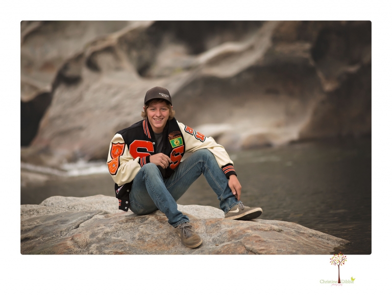 Summerville High School Senior portrait photographer Christine Dibble Photography takes four wheeling senior portraits of a boy with his trap gun, letterman jacket, and Toyota 4Runner as he drives over rocks and dives off cliffs.