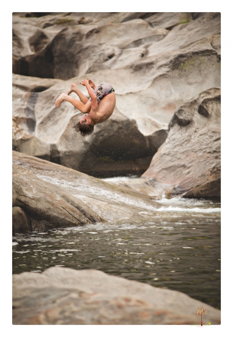 Summerville High School Senior portrait photographer Christine Dibble Photography takes four wheeling senior portraits of a boy with his trap gun, letterman jacket, and Toyota 4Runner as he drives over rocks and dives off cliffs.