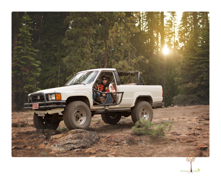 Summerville High School Senior portrait photographer Christine Dibble Photography takes four wheeling senior portraits of a boy with his trap gun, letterman jacket, and Toyota 4Runner as he drives over rocks and dives off cliffs.