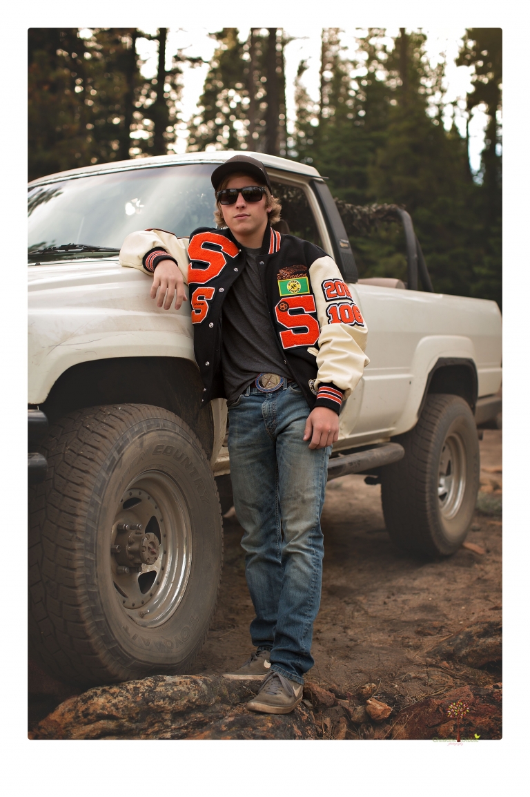 Summerville High School Senior portrait photographer Christine Dibble Photography takes four wheeling senior portraits of a boy with his trap gun, letterman jacket, and Toyota 4Runner as he drives over rocks and dives off cliffs.