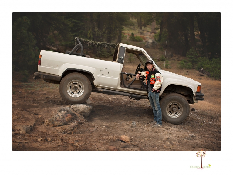 Summerville High School Senior portrait photographer Christine Dibble Photography takes four wheeling senior portraits of a boy with his trap gun, letterman jacket, and Toyota 4Runner as he drives over rocks and dives off cliffs.