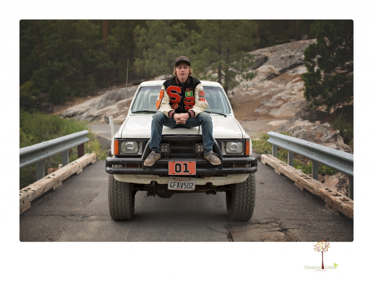 Summerville High School Senior portrait photographer Christine Dibble Photography takes four wheeling senior portraits of a boy with his trap gun, letterman jacket, and Toyota 4Runner as he drives over rocks and dives off cliffs.