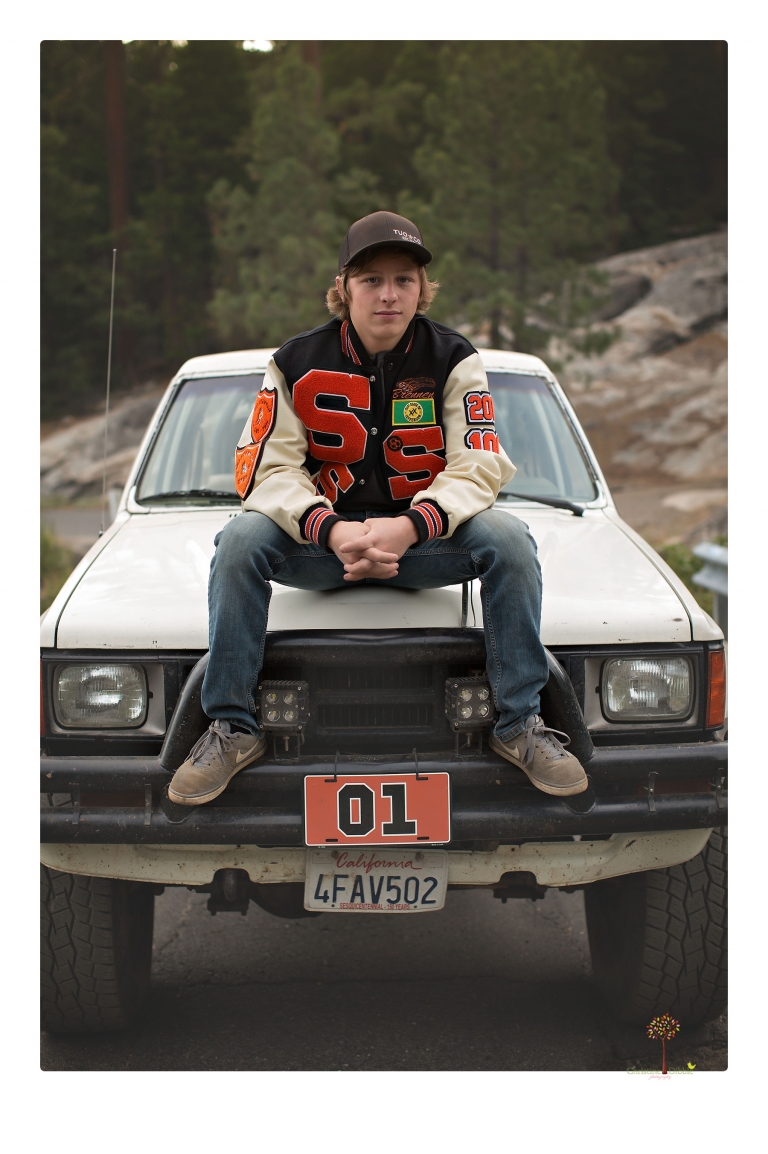 Summerville High School Senior portrait photographer Christine Dibble Photography takes four wheeling senior portraits of a boy with his trap gun, letterman jacket, and Toyota 4Runner as he drives over rocks and dives off cliffs.