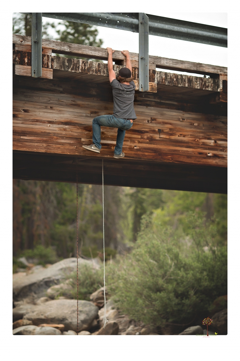 Summerville High School Senior portrait photographer Christine Dibble Photography takes four wheeling senior portraits of a boy with his trap gun, letterman jacket, and Toyota 4Runner as he drives over rocks and dives off cliffs.